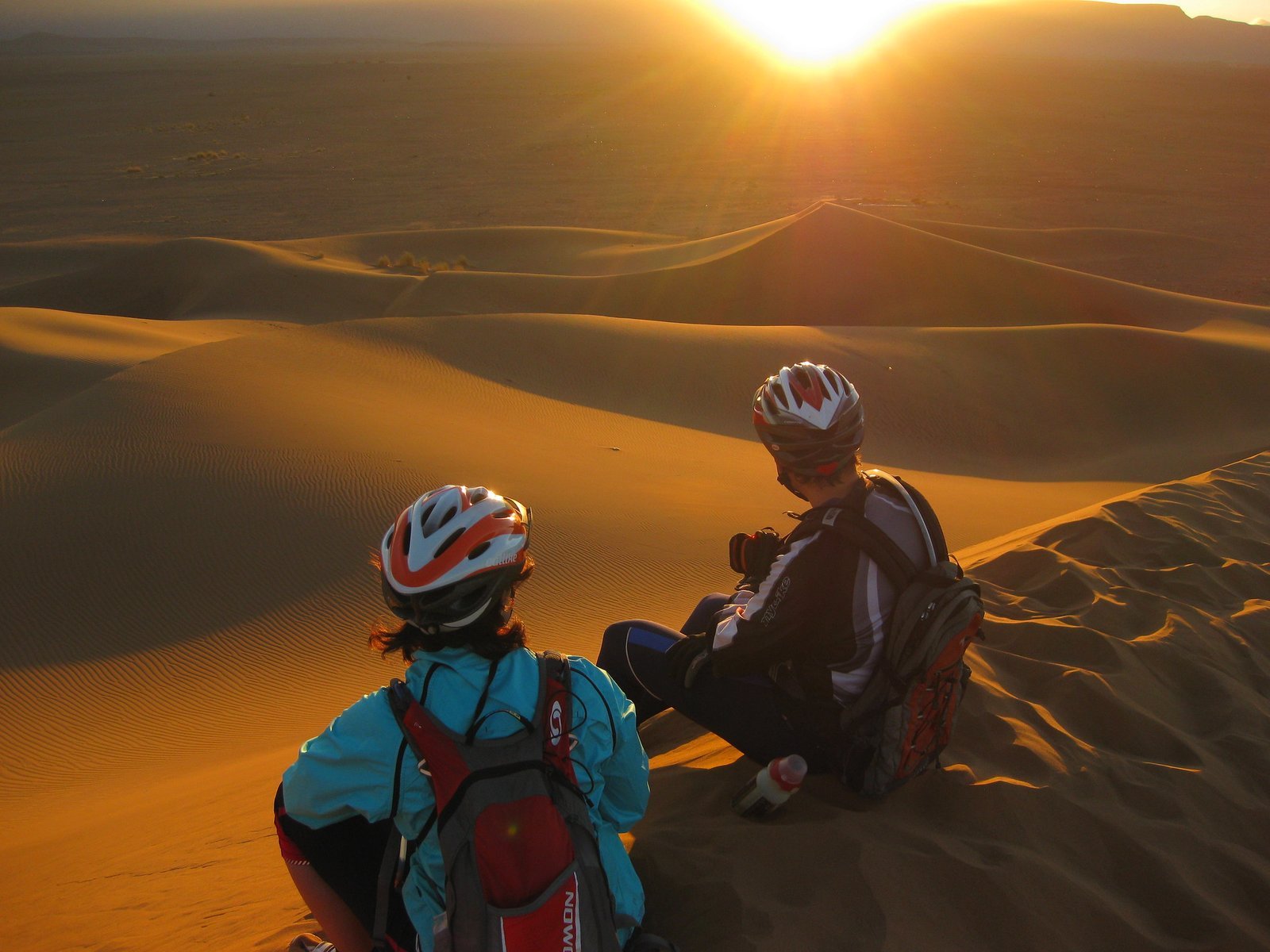 Cyclists riding through the Moroccan Sahara Desert landscape at sunset